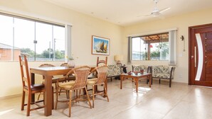 A dining area with a wooden table and chairs, a ceiling fan, and large windows.