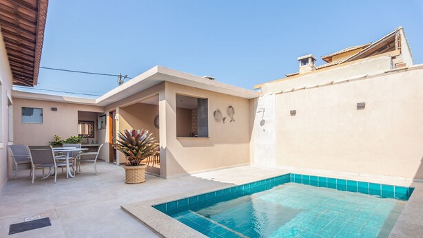 A modern outdoor pool area with a tiled deck, a dining set, and a small garden.