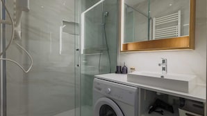 Een moderne badkamer met een douchecabine van glas, een wasmachine, een wastafel en een spiegel met houten lijst.