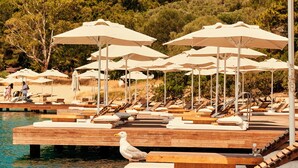 Een houten terras met lounge stoelen en parasols bij een zwembad, met uitzicht op een heuvel.