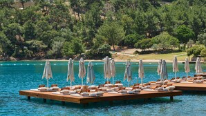 Een reeks houten vlotten met ligstoelen en parasols boven een wateroppervlak, omgeven door een beboste heuvel.