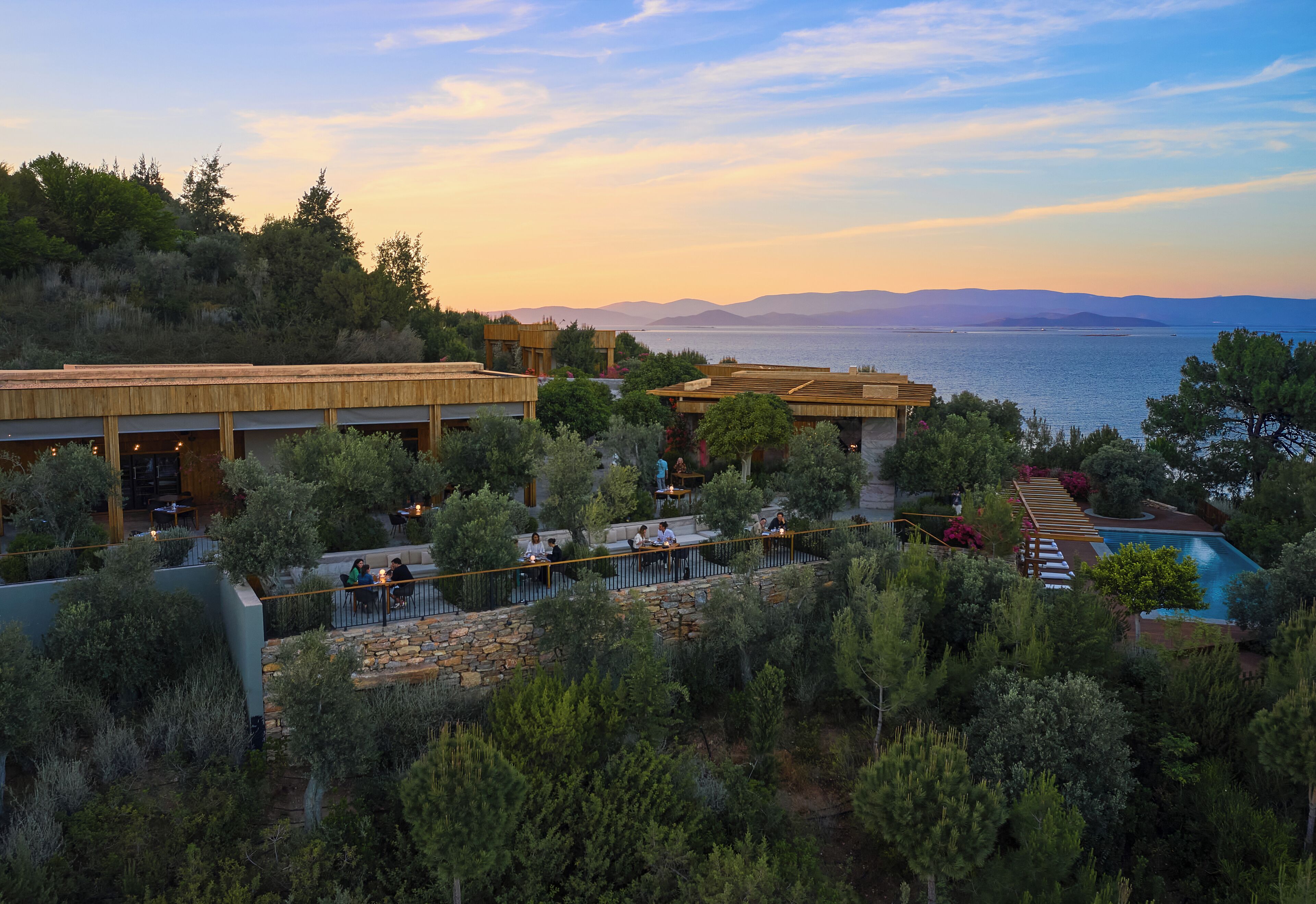 A resort with outdoor seating areas, a pool, and a view of the sea.