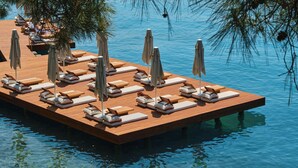 Een houten vlotter met ligstoelen en parasols boven het water.