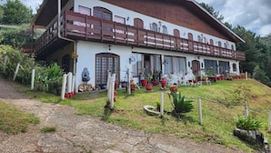 A large, two-story building with a balcony, surrounded by potted plants and a grassy area. - Pousada Cachyto de Cielo (Campos do Jordão)