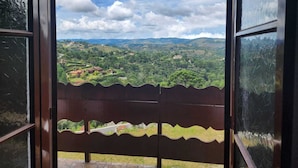 A view from a balcony with a wooden railing, overlooking a green landscape with hills and scattered buildings. - Pousada Cachyto de Cielo (Campos do Jordão)