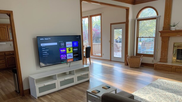 A modern living room with a flat-screen TV on a white stand, wooden flooring, a fireplace, and large windows. - Peaceful 3-bedroom accessible ranch home with AC, WiFi in Eastside Olathe. (Olathe)