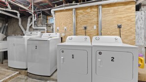 A laundry facility with two white washing machines labeled 1 and 2, connected to a wooden wall with visible electrical wiring.