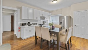 A modern kitchen with white cabinets, a stainless steel refrigerator, and a dining table with chairs.