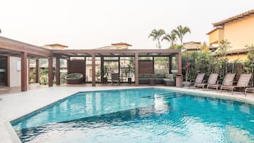 Piscina com espreguiçadeiras e área de estar coberta.