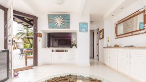 Un salón amplio con un televisor grande, armarios blancos y una mesa de centro de cristal con un objeto decorativo.