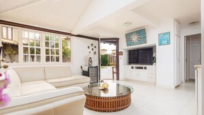 Un salón amplio con un sofá blanco, una mesa de centro de vidrio y un objeto decorativo, y un televisor.