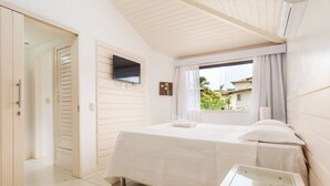Un dormitorio con cama, ventana con cortinas, televisor montado en la pared y una mesita de noche.