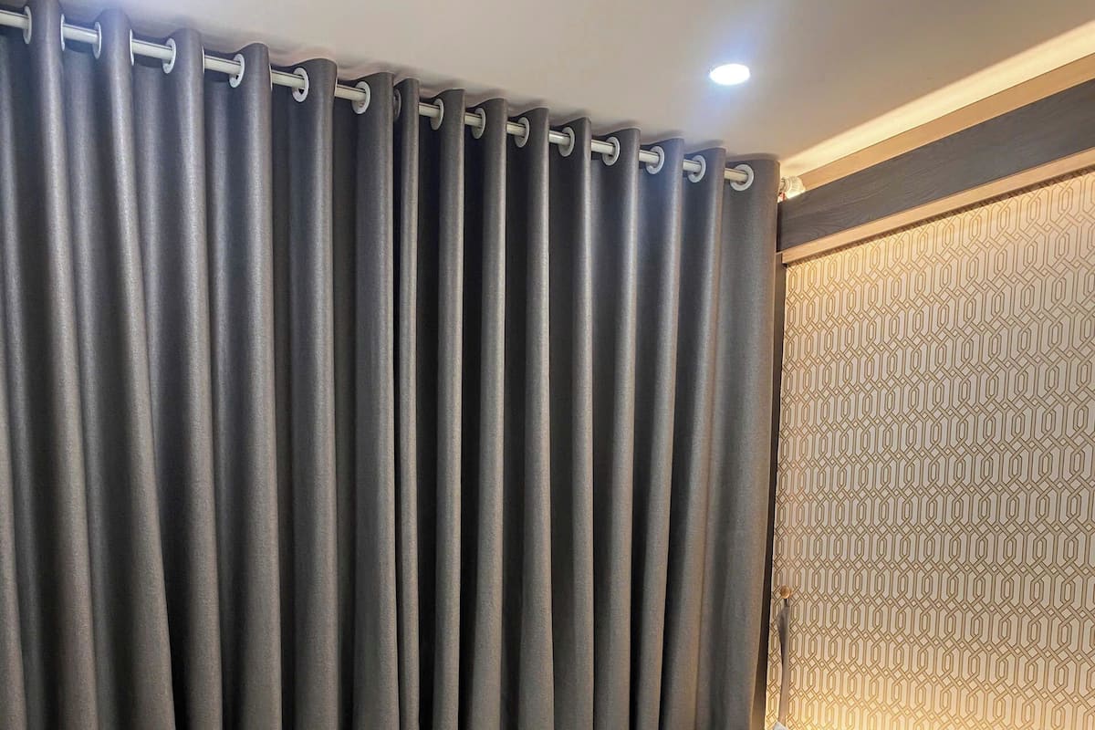 A hotel room with a bed, curtains, a patterned wall, and a wooden floor.