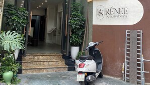 The entrance of a hotel with a glass canopy, a sign for 'Renee Beauty Room', and a parked scooter. - Royal Lotus Apartment and Hotel Ha Noi (Hanoi)