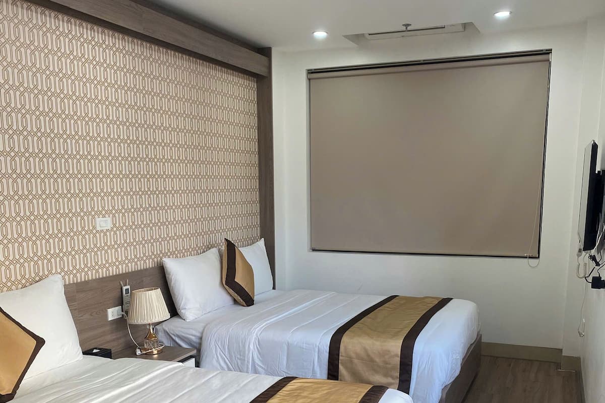 A hotel room with two beds, a patterned wall, a large window, and a flat-screen TV.