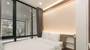 A modern hotel room with a large bed, a window with curtains, a patterned wall, and a bedside table with a lamp. - Royal Lotus Apartment and Hotel Ha Noi (Hanoi)