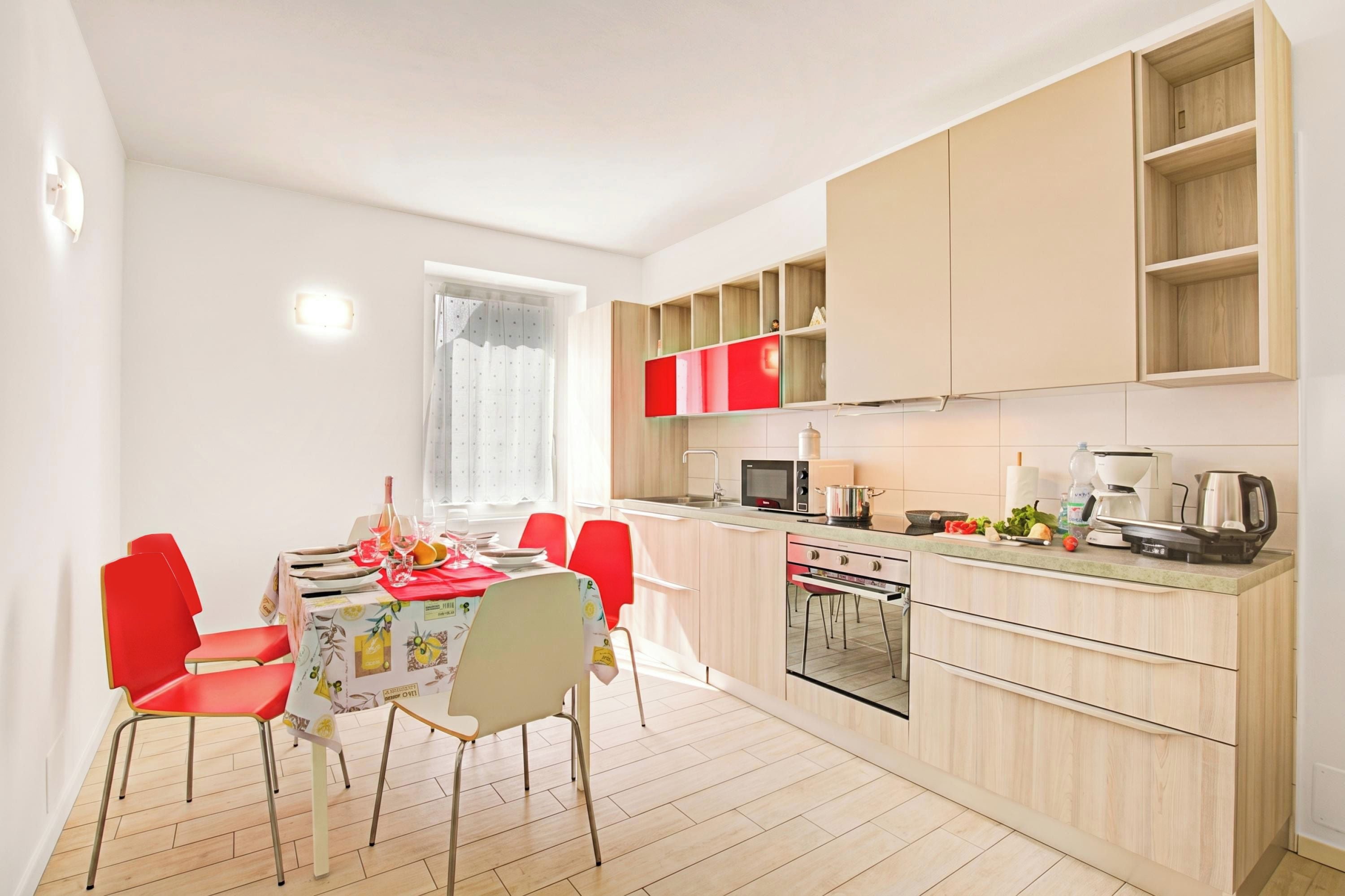 Una cocina compacta con armarios de madera, una mesa de comedor con sillas rojas y un microondas.
