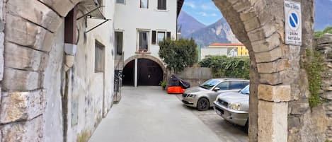 Una calle estrecha con un arco de piedra, un edificio con un portón negro y un cartel que indica zona de estacionamiento prohibido.