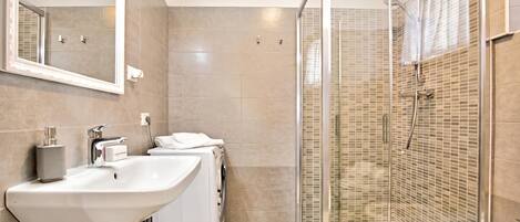 A modern bathroom with a large sink, a washing machine, a shower with glass doors, and a mirror.
