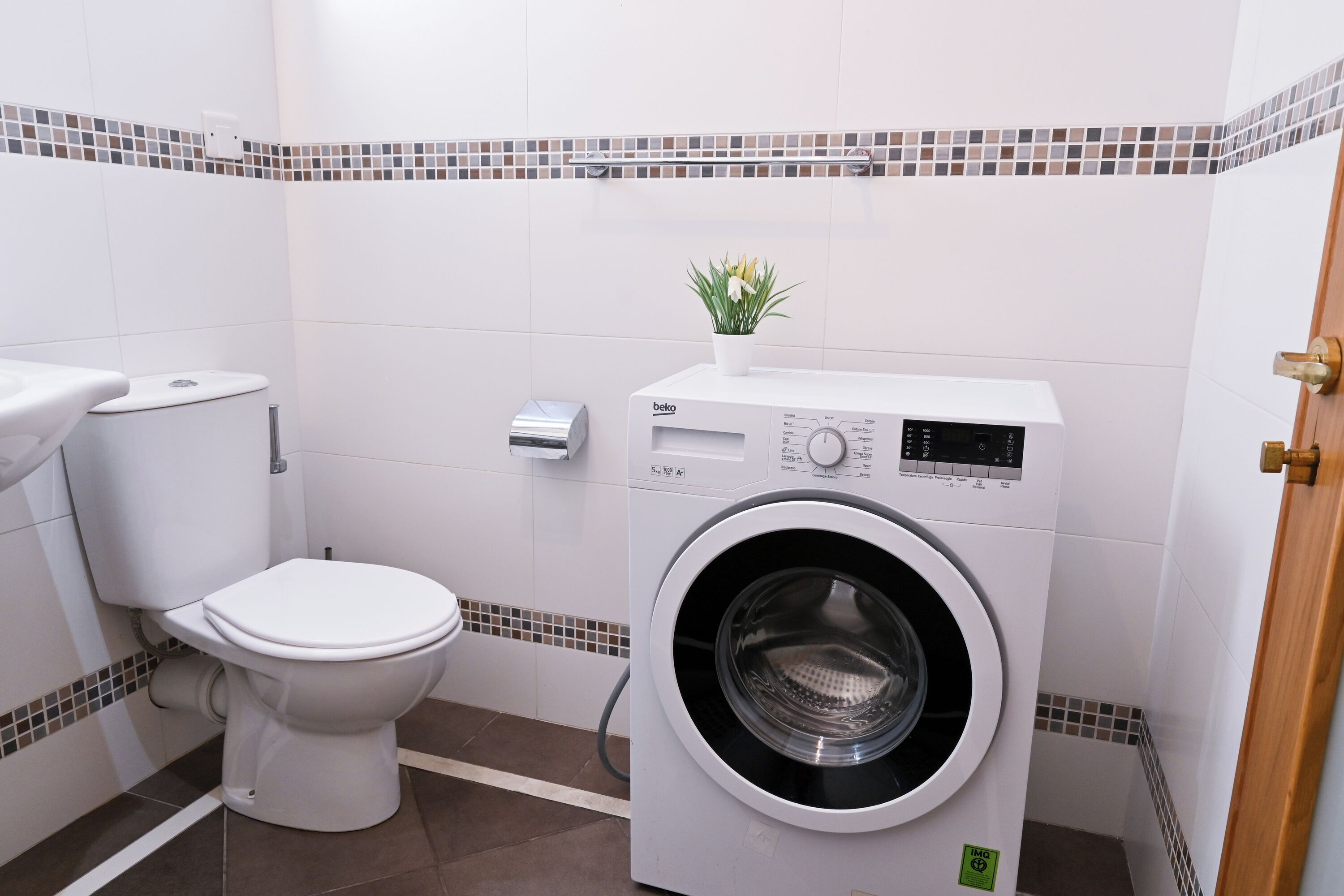 Un baño pequeño con inodoro, lavadora y una planta en maceta.