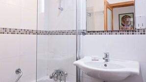 Un bany amb dutxa de vidre, un lavabo i un mirall amb marc decoratiu.