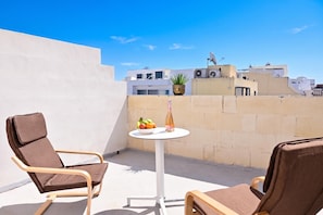 Eine Dachterrasse mit zwei Liegestühlen, einem kleinen Tisch mit Früchten und einer Flasche sowie einem Blumentopf.