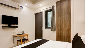 A bedroom with a bed, a desk with a chair, a television, a wardrobe, and an air conditioning unit.