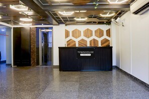 A reception area with a sign reading 'TOWNHOUSE' and a 'Company-Serviced' label. There is a reception desk, a wall with geometric wooden panels, and a polished floor. - Classic Rohini Sector 18 Known as Relic (New Delhi)