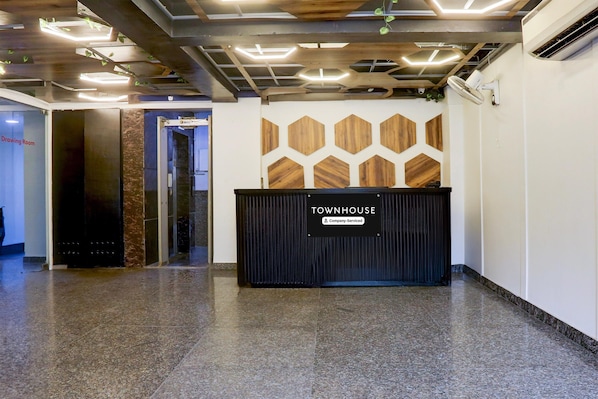 A reception area with a sign reading 'TOWNHOUSE' and a 'Company-Serviced' label. There is a reception desk, a wall with geometric wooden panels, and a polished floor.