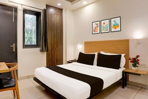 A hotel room with a bed, a desk, a chair, a nightstand, a phone, and a wall with three framed pictures. - Classic Rohini Sector 18 Known as Relic (New Delhi)