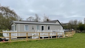 A single-story mobile home with a deck, white railings, and a small porch. - Caravan in Holcot - Sleeps 6 - Maximum 6 People - Maximum 4 Adults per Booking -pet Friendly (Northampton)