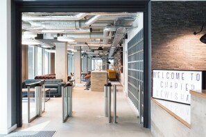 An interior corridor with a reception desk, seating area, and a view of the outside. - Chapter Lewisham Student Only Cozy Stay (London)