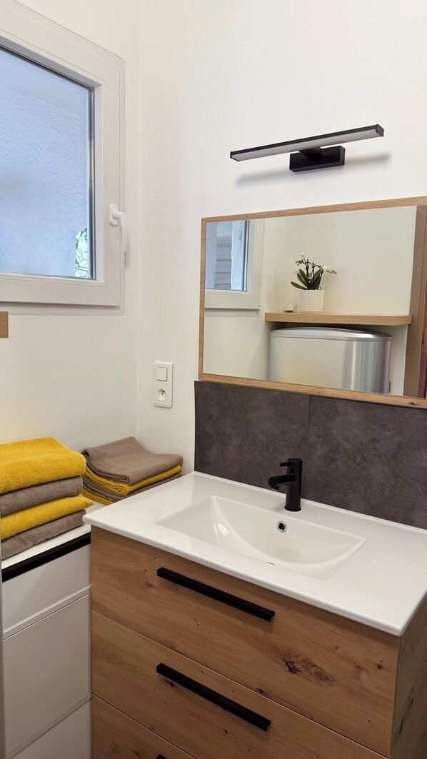 Un baño moderno con un lavamanos blanco, un mueble de madera y un espejo encima.