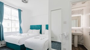 A hotel room with two beds, a window with curtains, a mirror, a sink, and a hairdryer. - Whiteleys Hotel (London)