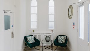 A spacious room with a high arched ceiling, a chandelier, two green armchairs, a small table, and a black doormat. - Whiteleys Hotel (London)