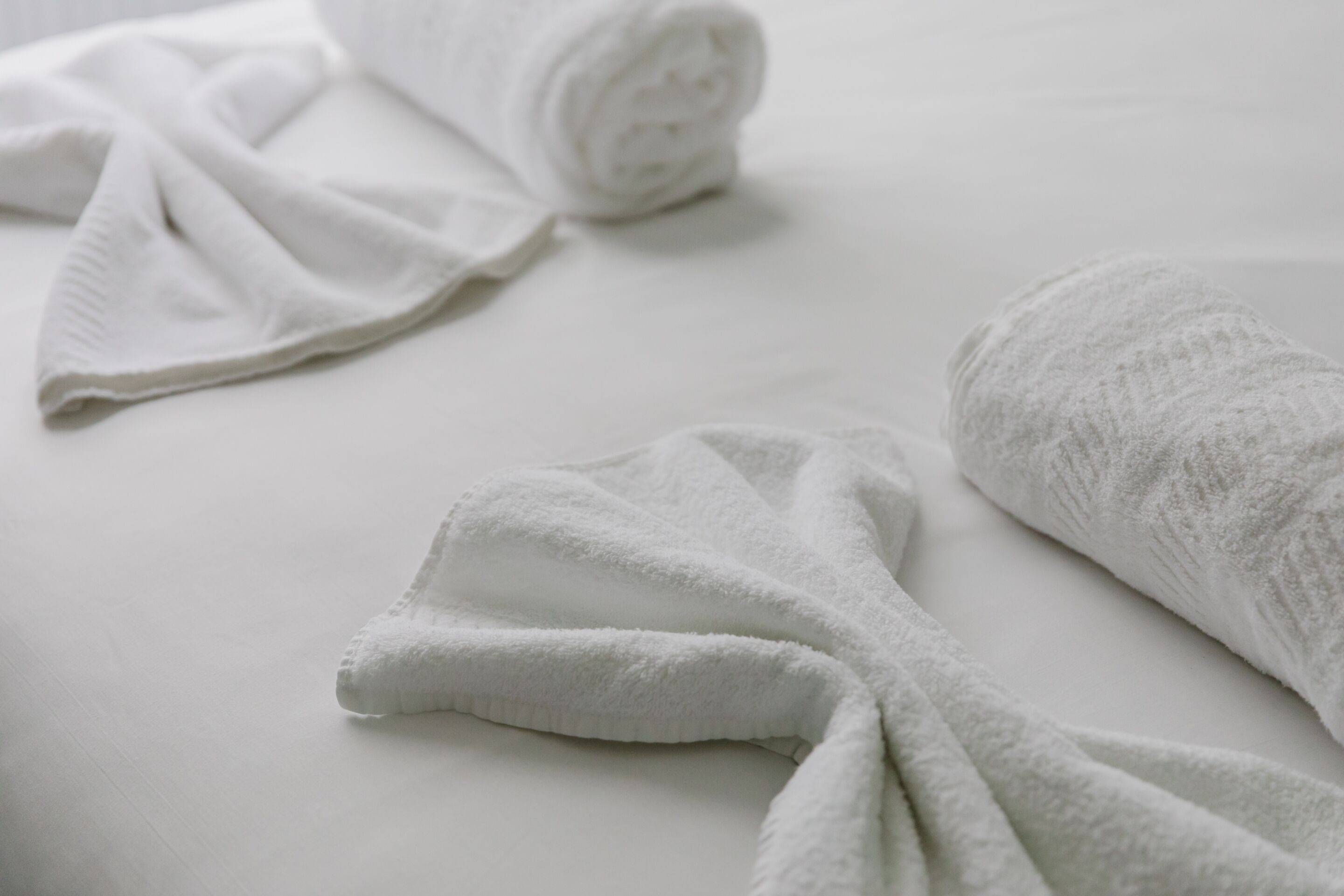 Un lit bien fait, avec du linge de lit blanc, comprenant une serviette enroulée et une autre pliée.