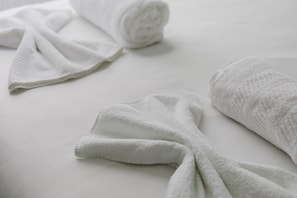 A neatly made bed with white linens, including a rolled-up towel and a folded one.