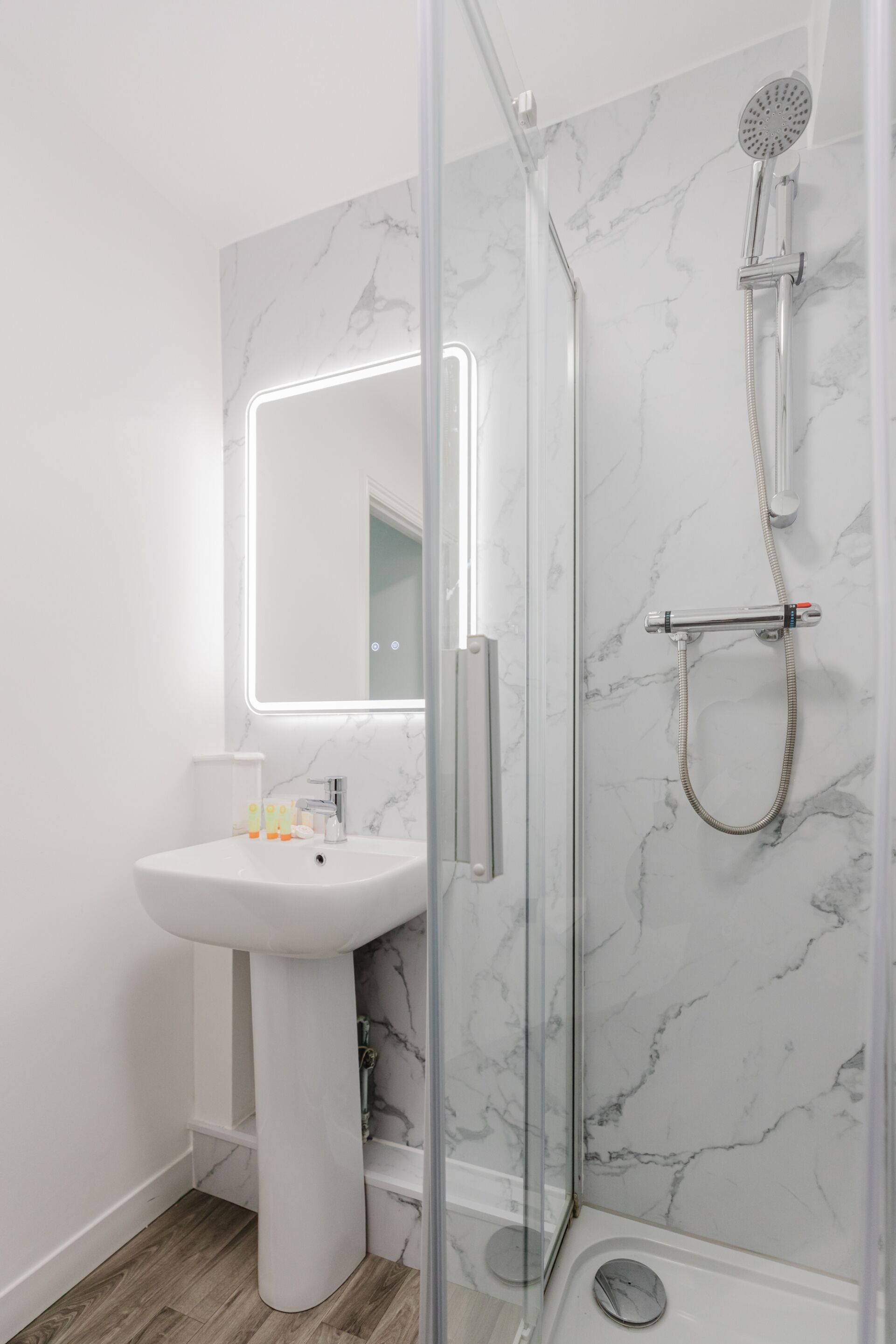 A bathroom with a white pedestal sink, a glass shower enclosure, and a marble wall.
