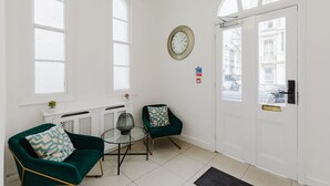 A room with a green chair, a small table, a clock, and a door with a view of the street. - Whiteleys Hotel (London)
