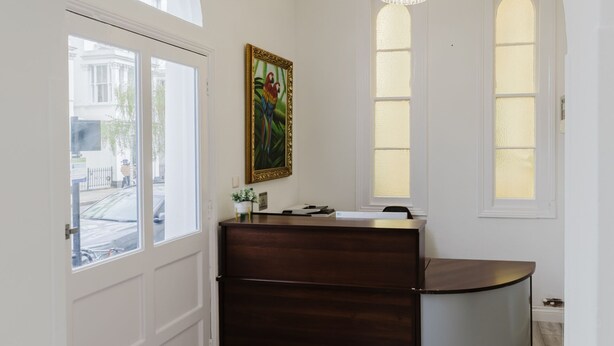 A room with a white door, a reception desk, a chandelier, and a painting on the wall. - Whiteleys Hotel (London)