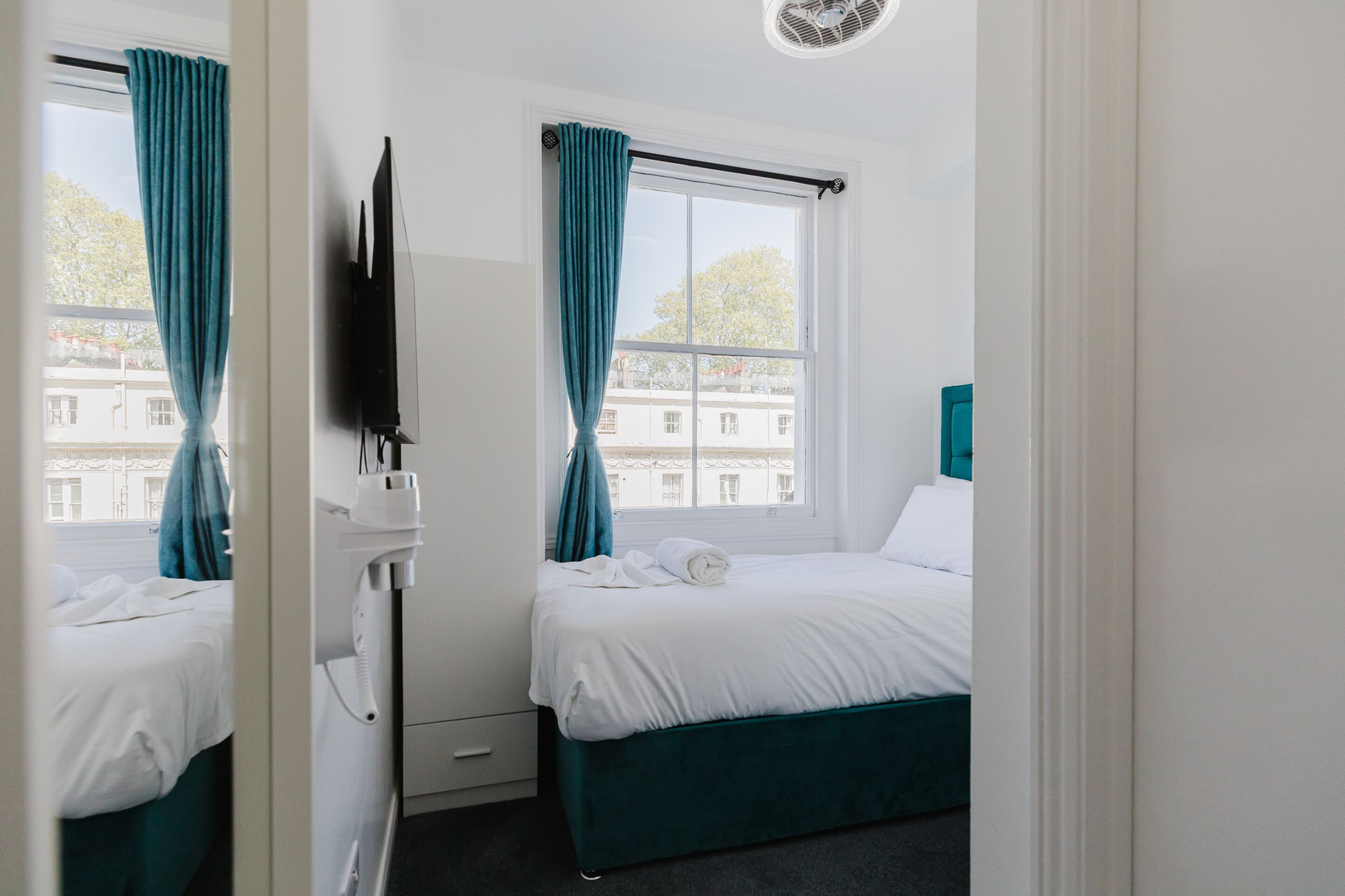 A hotel room with a bed, a TV, a phone, and a window with curtains.