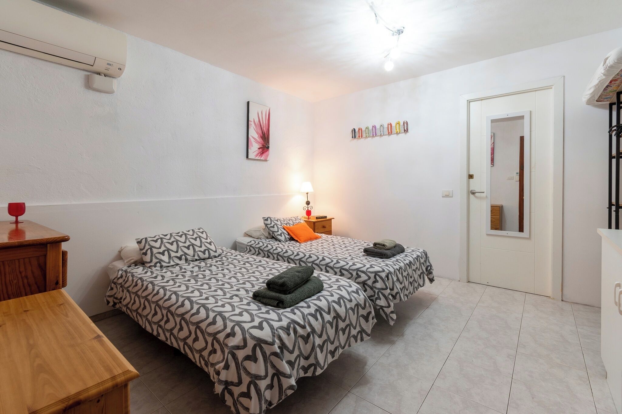 A small, clean room with two beds, a wooden table, a lamp, and a door.