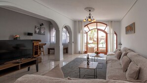 A living room with a TV, sofa, coffee table, and a view of the outside. - Villa Tricia 6 Bedroom Las Americas (Arona)