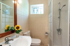 A bathroom with a sink, toilet, and shower. There is a window above the toilet and a mirror above the sink.