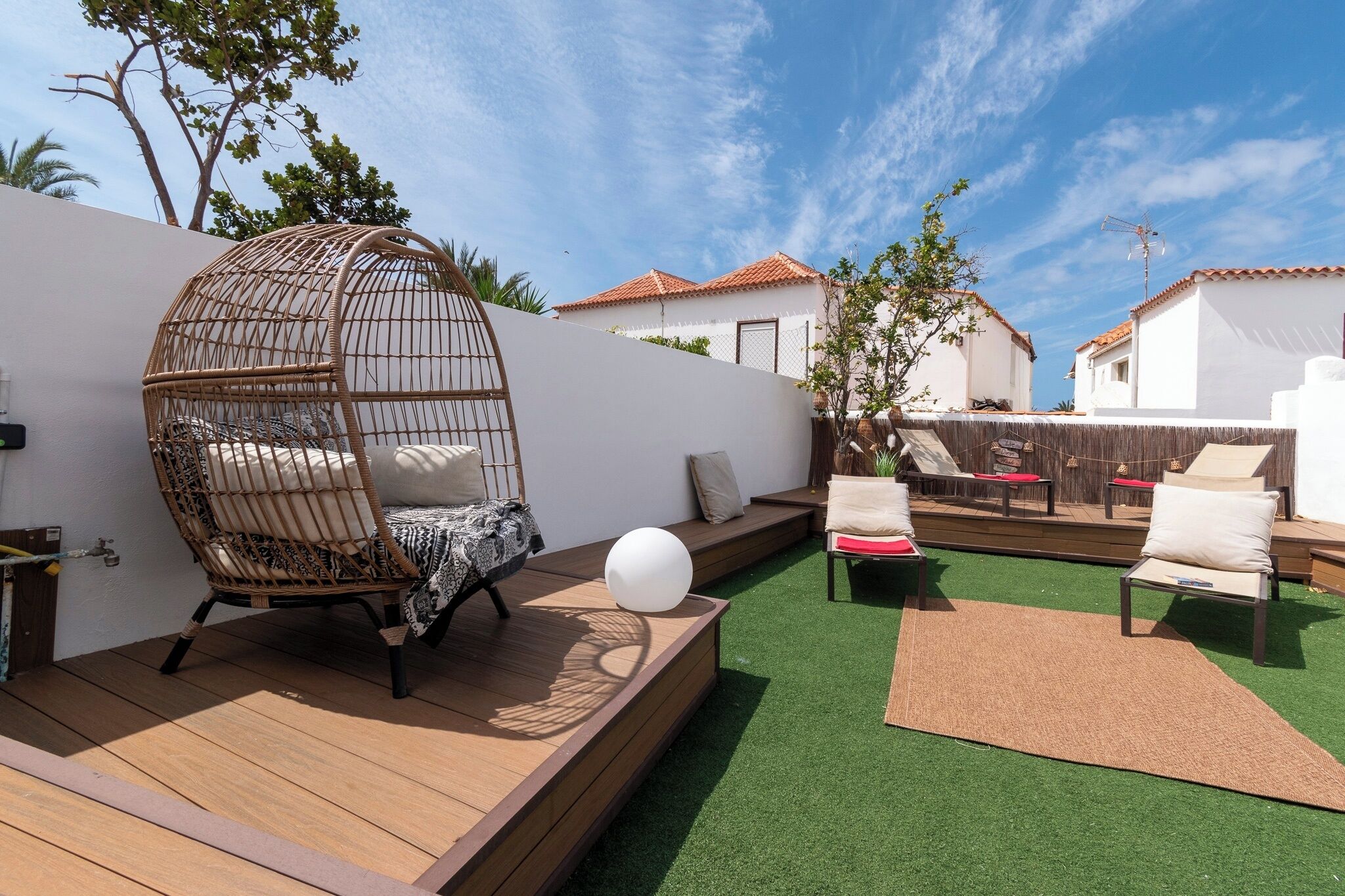 A rooftop terrace with a wicker chair, a white spherical object, and outdoor seating.