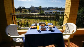 A balcony with a table set for breakfast, overlooking a road and buildings. - Stavros Apartments Gouvia Marina (Corfu)