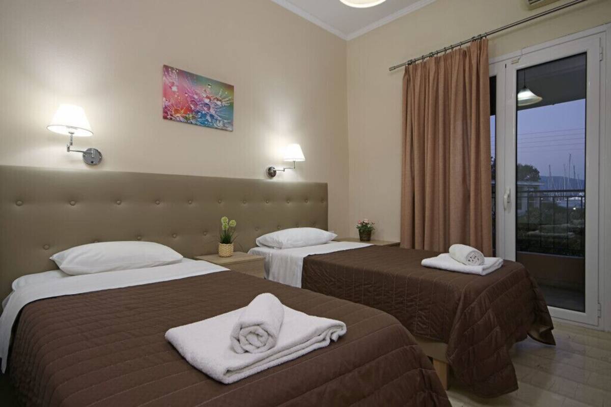 A hotel room with two beds, a large window with curtains, and a painting on the wall.