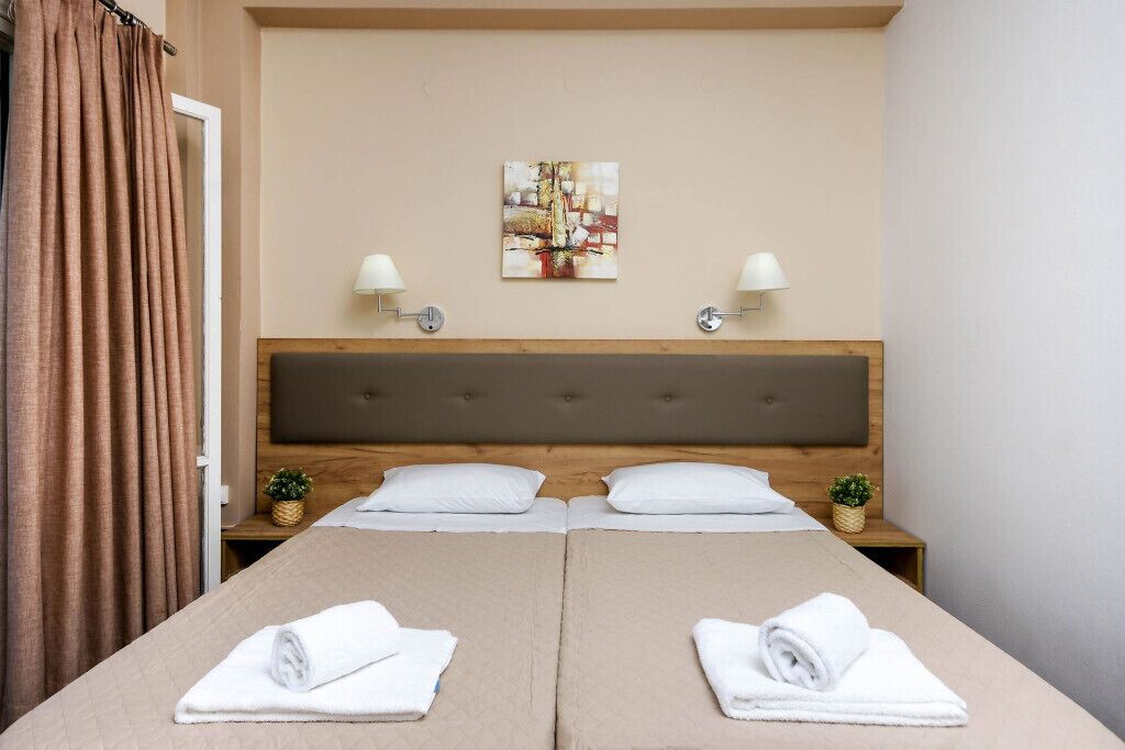 A hotel room with a double bed, two bedside tables, a headboard, a painting on the wall, and two lamps.
