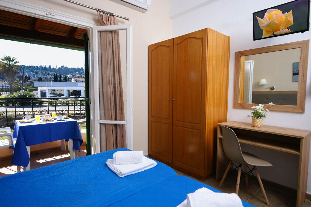 Une chambre d’hôtel comprenant un lit, un bureau, une chaise, une armoire, un balcon avec une table et des chaises, et une vue sur l’extérieur.