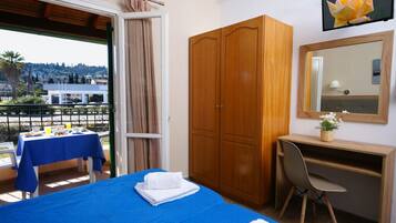 Une chambre d’hôtel comprenant un lit, un bureau, une chaise, une armoire, un balcon avec une table et des chaises, et une vue sur l’extérieur.
